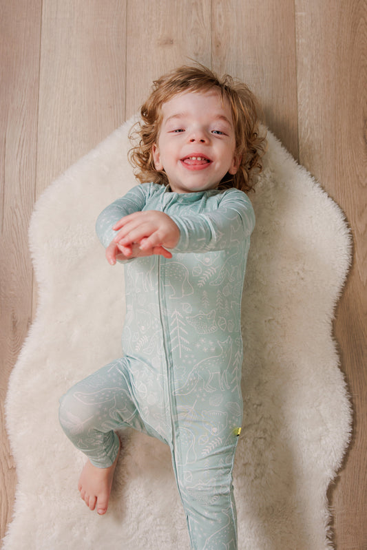 Child wearing a light blue onesie on a white rug with a wooden floor background