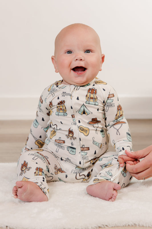 Baby wearing a patterned onesie sitting on a white rug with a blurred background