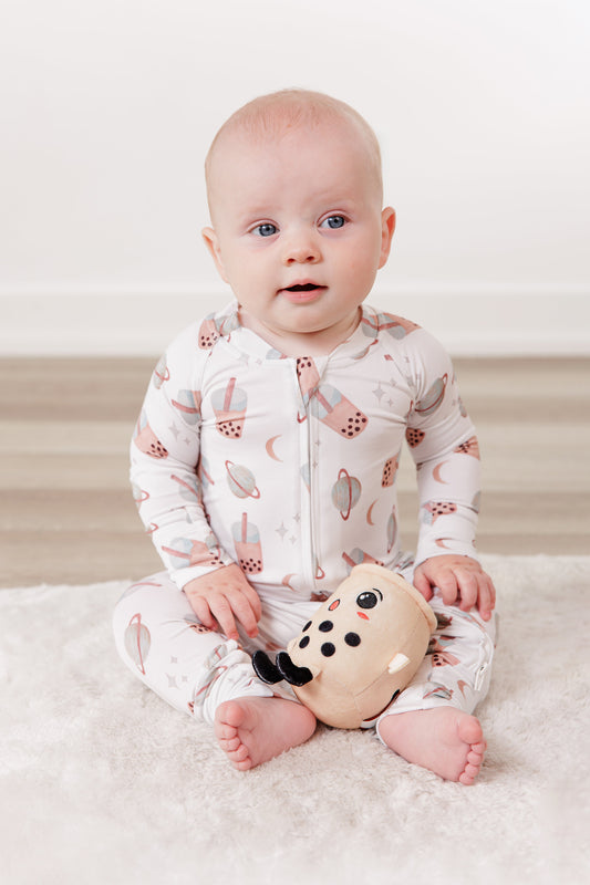 Baby in a patterned onesie holding a toy on a white blanket