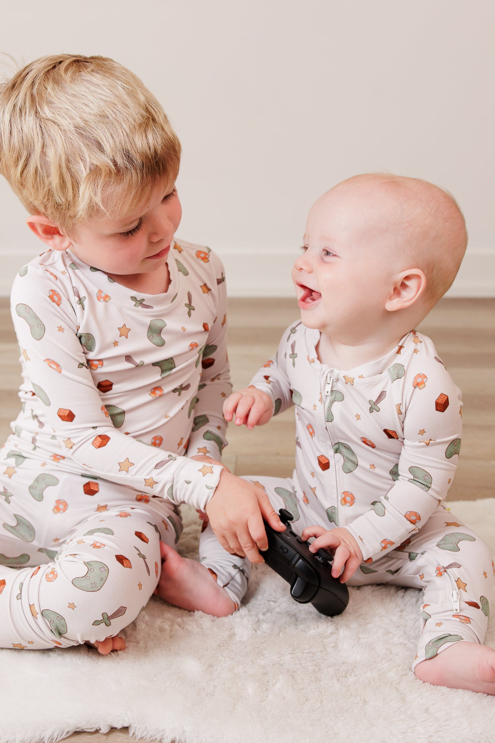 Two children in matching pajamas sitting on a white rug.
