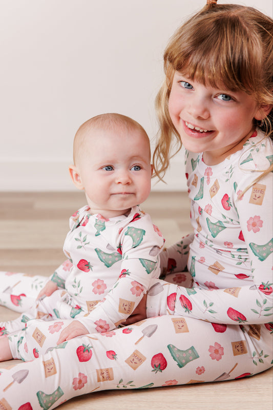 Two children wearing matching pajamas with a pattern of apples and boxes on a wooden floor.