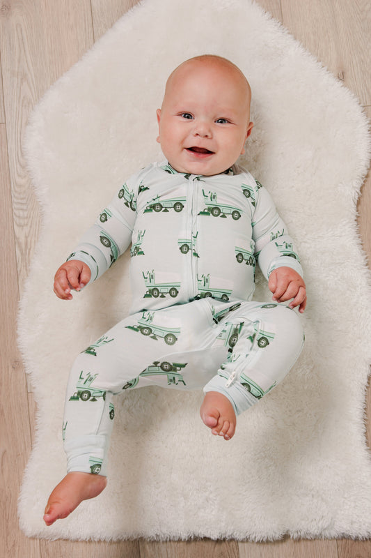 Baby wearing a green and white pajama set with vehicle pattern on a white rug.